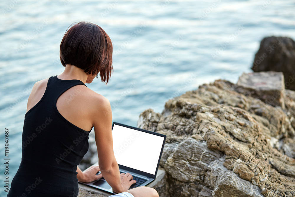 Beautiful young freelancer woman using laptop sitting near the sea.Happy smiling girl working online.Studying and learning using notebook computer.Freelance work,business people concept.