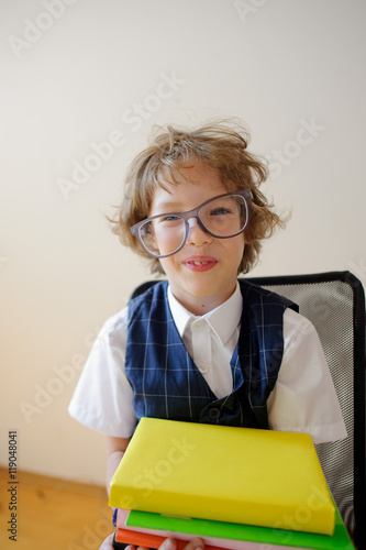 Disheveled little schoolboy holding a stack of textbooks and smiles.