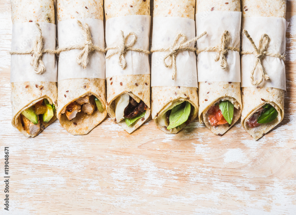 Tortilla wraps with various fillings on shabby painted board over white