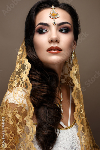 Beautiful girl in Indian style with a scarf on her head. Model with a creative and bright makeup. Beautiful face. The photo was taken in a studio.