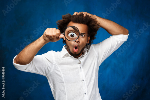 Photos Young handsome african man posing with magnifier over blue background
