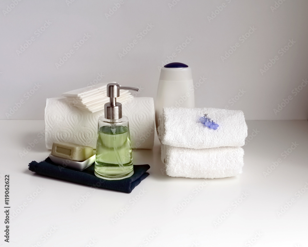 Part of a spa interior. Paper and cotton napkins, tissue, towels, soap and cosmetic products on a wooden table. White background and table, toned image. copy space Part of a spa interior. Paper and cotton napkins, tissue, towels, soap and cosmetic products on a wooden table. White background and table, toned image. copy space