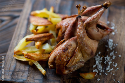 Close-up of whole roasted quails served with potato wedges
