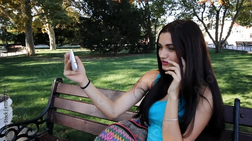 young beautiful brunette woman in a blue t-shirt is photographed selfie on a mobile phone while sitting in a park on a walk photo