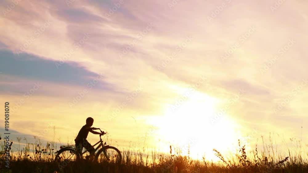 9 yeard old boy riding bike then celebrating his success with funy dance. Silhouette of little jumping happy kid with hands up at sunset sky background. Real time bideo footage. 9 yeard old boy riding bike then celebrating his success with funy dance. Silhouette of little jumping happy kid with hands up at sunset sky background. Real time bideo footage.