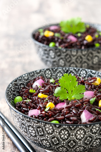 Black rice in a bowl and vegetables on wooden table