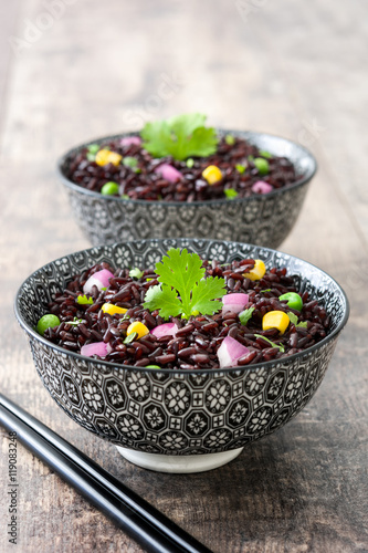 Black rice in a bowl and vegetables on wooden table