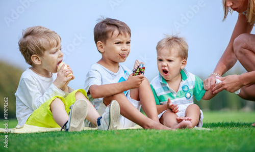 Obraz na plátně Two older boys eating ice cream, young woman wiping hands of youngest son