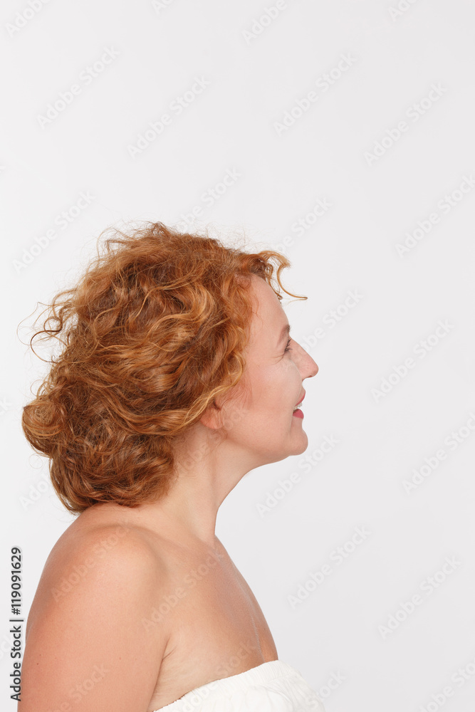 Profile of happy red haired mature or middle aged woman looking away while posing isolated on white background in studio. Profile of happy red haired mature or middle aged woman looking away while posing isolated on white background in studio.