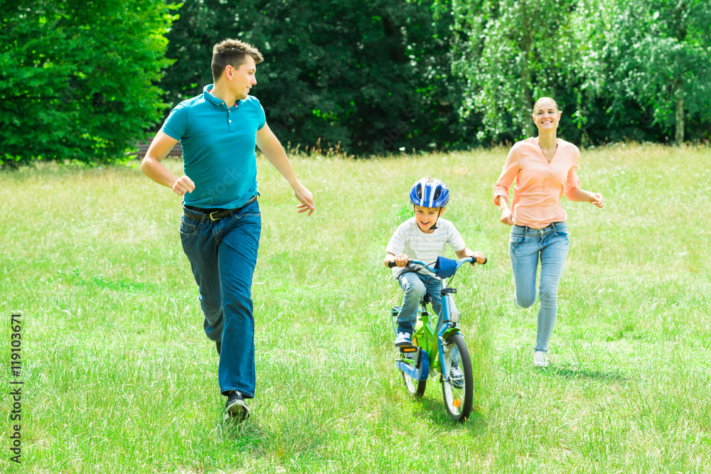 Parents Running With Their Son Riding A Bicycle Parents Running With Their Son Riding A Bicycle