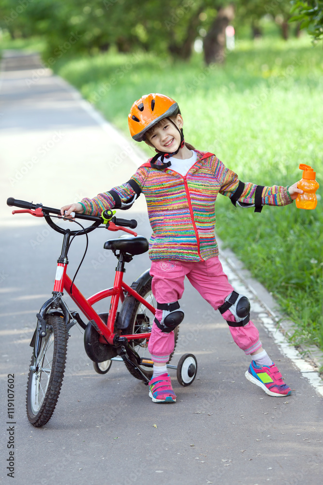 Fototapeta premium little girl with a bike and a bottle of water in hand