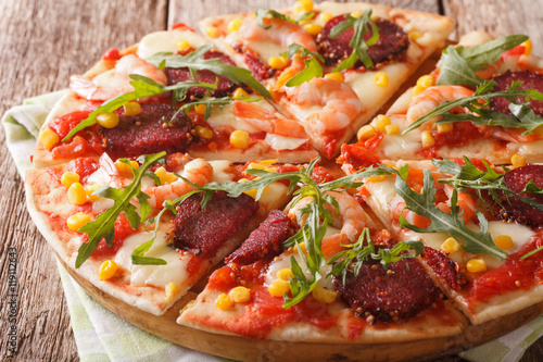 Hot pizza with shrimp, salami, cheese and arugula close-up on a wooden. horizontal 