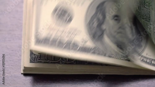 A large stack of hundred dollar bills on a table gradually blows away to nothing.