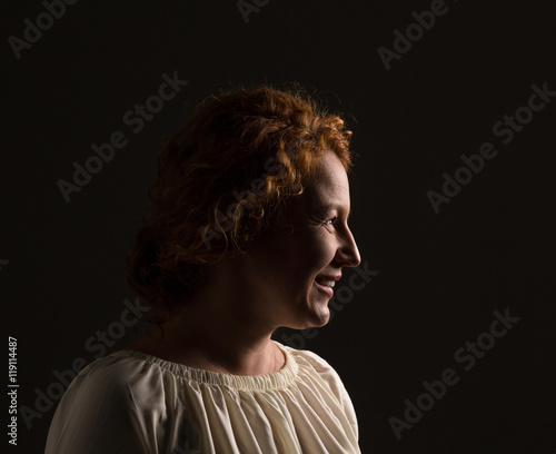 Profile of middle aged woman with red hair in studio. Happy mature or senior woman looking away isolated on black background.