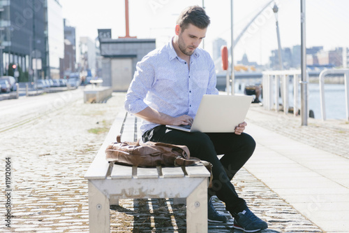 Ireland, Dublin, young businessman sitting on bench using laptop photo