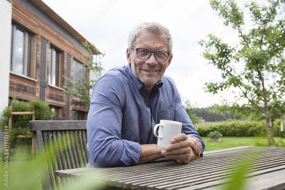 Portrait of confident mature man with cup at garden table Portrait of confident mature man with cup at garden table