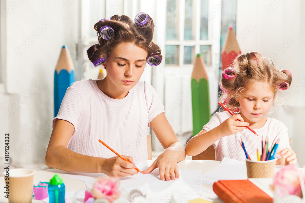 Fototapeta premium The young mother and her little daughter drawing with pencils at home