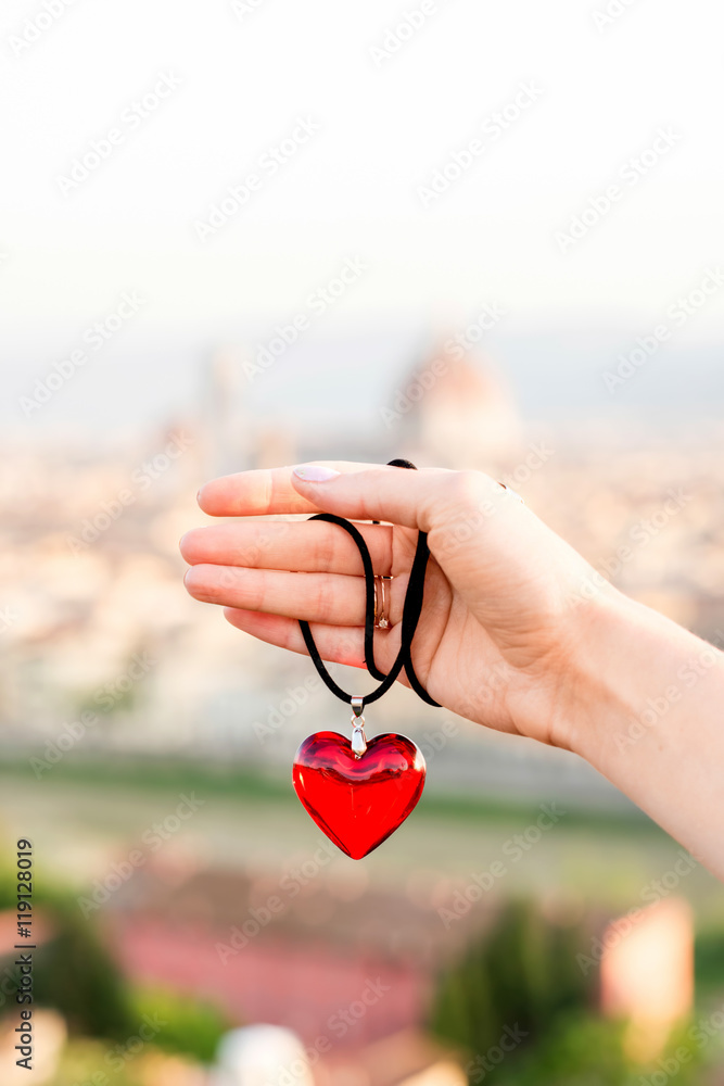 Fototapeta premium Female hand holding pendant in form of the heart on the old town background in Florence