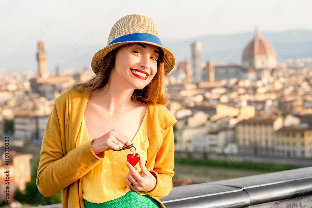 Young smiling woman in yellow holding pendant in form of the heart on the old town background in Florence