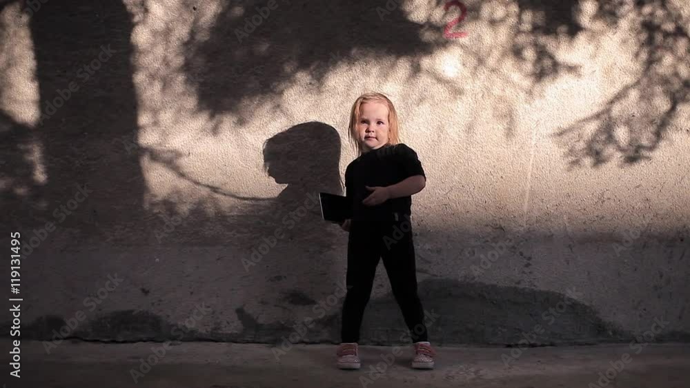 Funny Little Girl Posing on a Background of a Concrete Sunny Wall Then Typing Something on the Tablet and Displays it Into the Camera Funny Little Girl Posing on a Background of a Concrete Sunny Wall Then Typing Something on the Tablet and Displays it Into the Camera