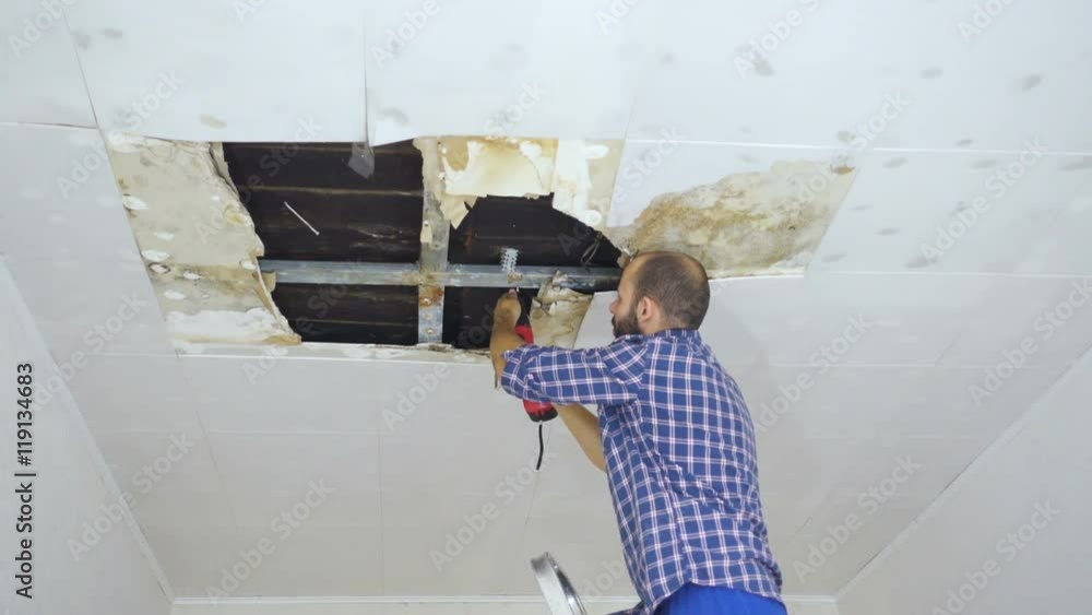Man repairing collapsed ceiling. Ceiling panels damaged huge hole in roof from rainwater leakage.Water damaged ceiling . Man repairing collapsed ceiling. Ceiling panels damaged huge hole in roof from rainwater leakage.Water damaged ceiling .