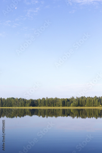 Calm morning. The forest is reflecting from the still water during sunrise. 