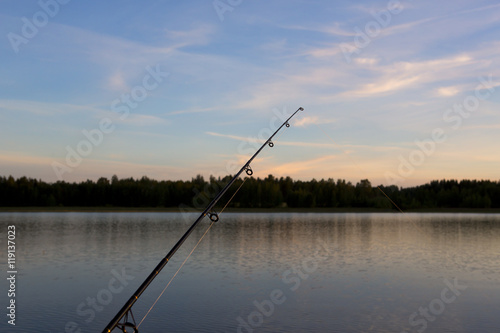 Fishing at the night time in Finland. An image of a fishing rod and line against a colorful sunset. The sky and water is glowing yellow.