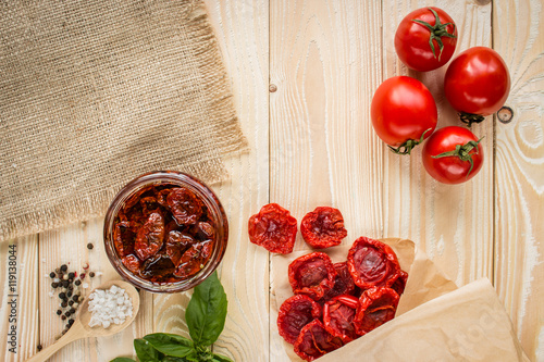 Fototapeta Naklejka Na Ścianę i Meble -  tomato fruits, dried tomatoes, dried  tomatoes in olive oil at jar, basil leaf, and salt in wooden spoon on wooden table. top view