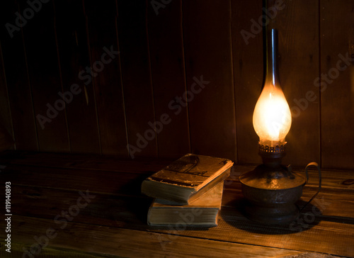 Old antique books with burning paraffin lamp near on the wooden table.
