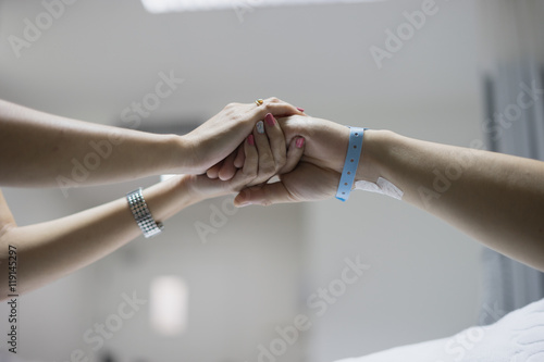 hand of man and woman couple in hospital and patient bed with hospital tag on wrist with love hope and care