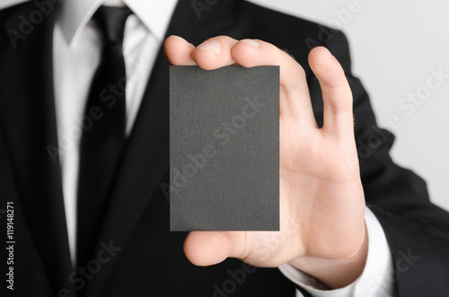 Fototapeta Naklejka Na Ścianę i Meble -  Black Business Card Mock-Up (85x55mm) - Man in a black suit holding a black card on a gray background.