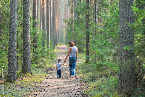Mother and baby walk on country rural road in pine forest