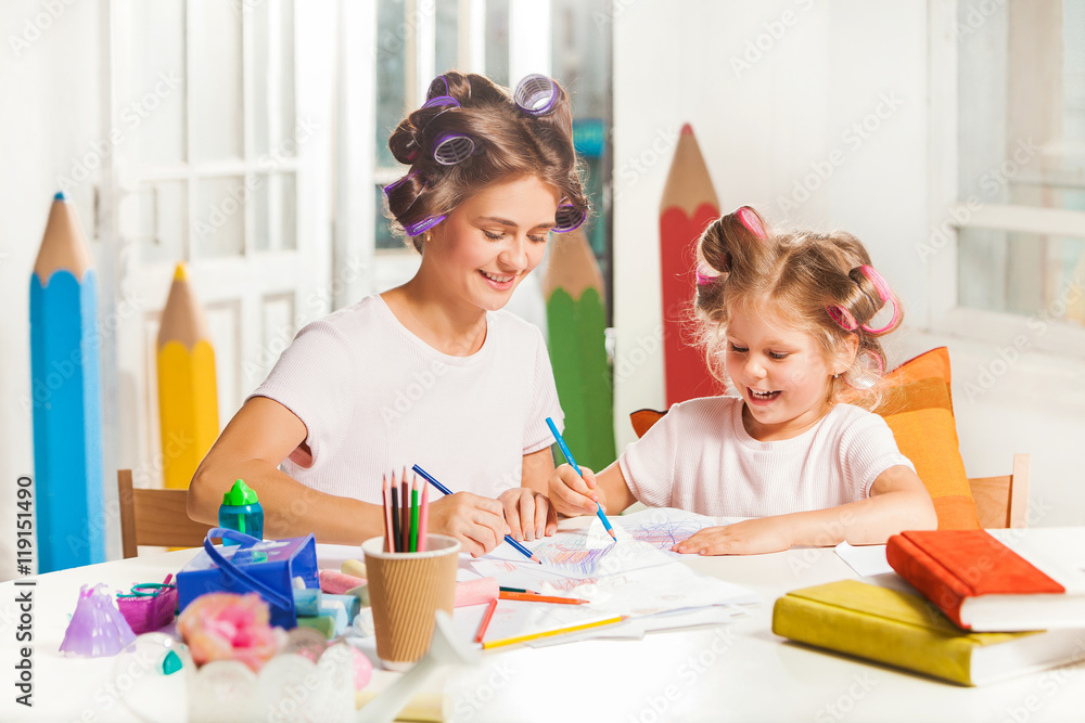 Fototapeta premium The young mother and her little daughter drawing with pencils at home