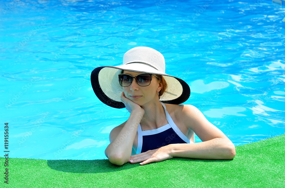 Beautiful young woman in a sun hat and sunglasses on edge of poo