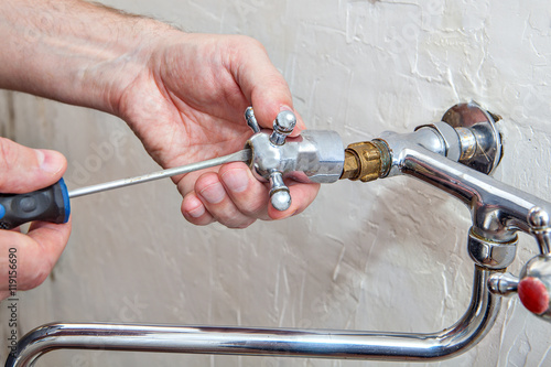 Plumbing repair, plumber unscrews handle kitchen faucet using screwdriwer photo