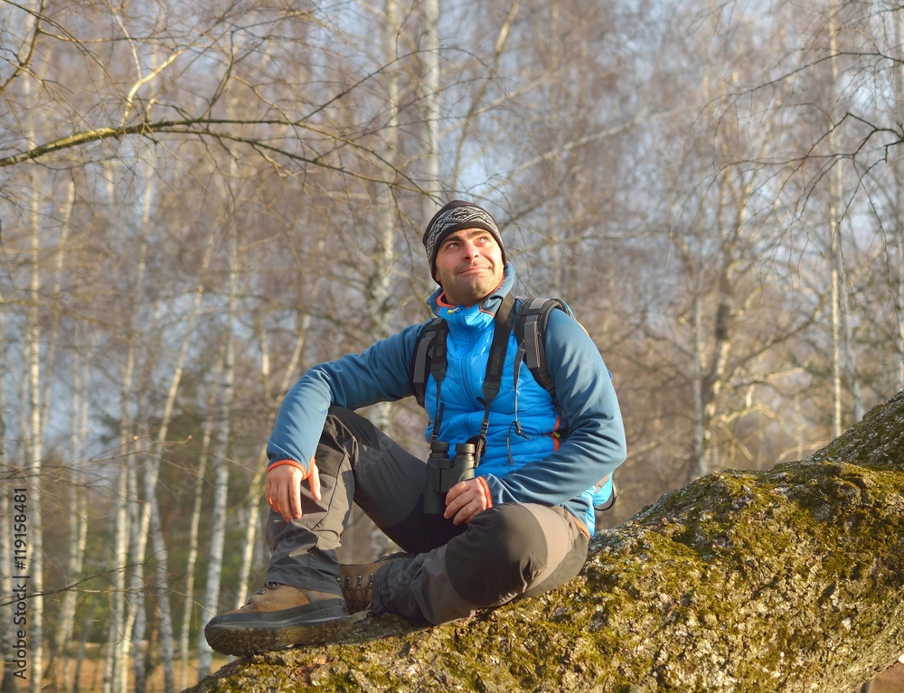 Obraz premium man with backpack hiking resting on a trunk in forest