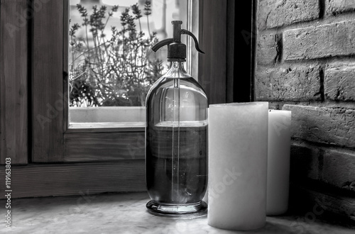 Obraz na plátně Old soda siphon and white candle on windowsill near brick wall