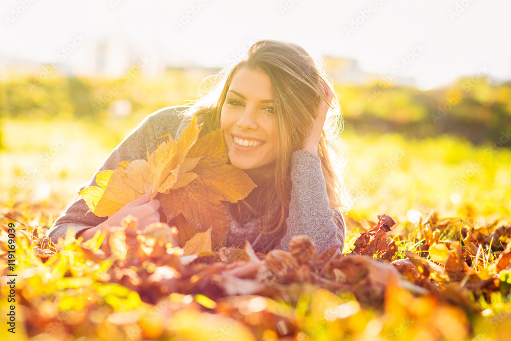 Cheerful beautiful young woman lying in park in autumn holding leaves Cheerful beautiful young woman lying in park in autumn holding leaves