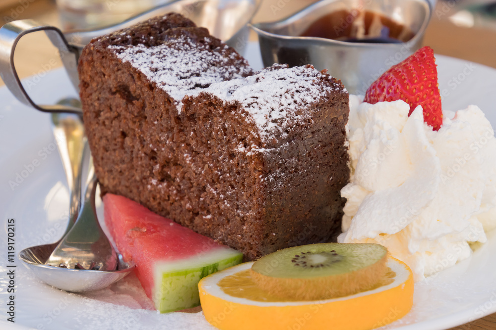 Delicious chocolate cake with whipped cream, garnished with fruits Delicious chocolate cake with whipped cream, garnished with fruits