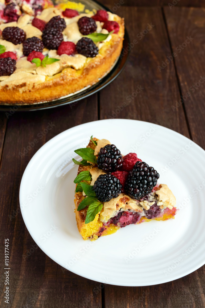A piece of the pie (Tart) with fresh blackberries and raspberries, air meringue, mint decoration on a white plate A piece of the pie (Tart) with fresh blackberries and raspberries, air meringue, mint decoration on a white plate
