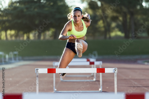 Young athlete jumping over a hurdle during training on race trac photo