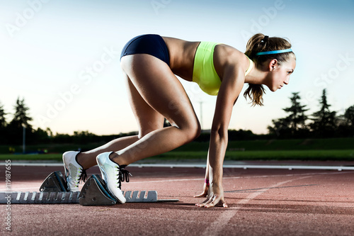 Canvas Print Young female athlete launching off the start line in a race.