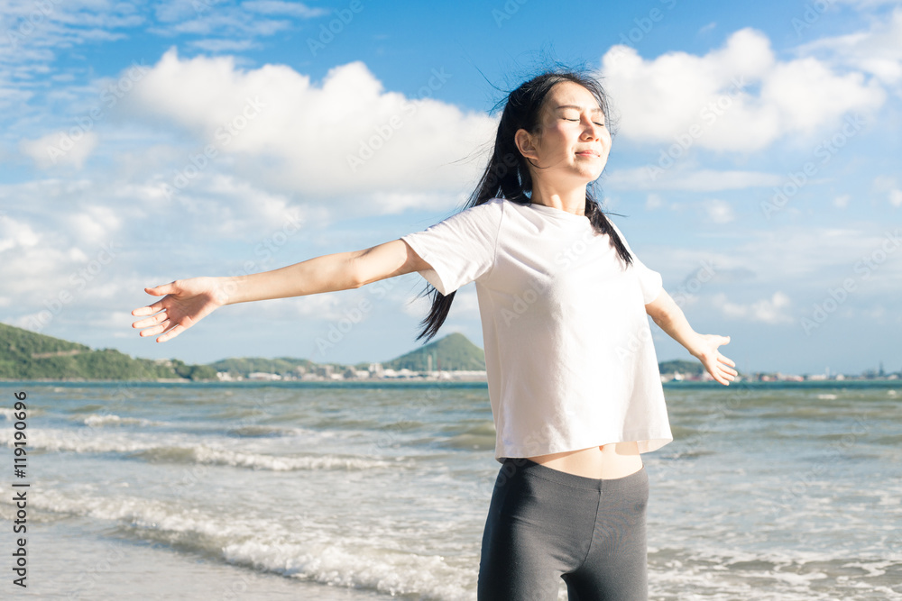Happy relaxed asian woman breathing deep fresh air and raising arms on the beach with blue sky background Happy relaxed asian woman breathing deep fresh air and raising arms on the beach with blue sky background
