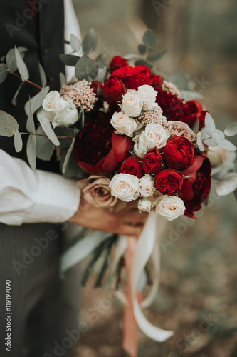 Portrait of a wedding groom posing with bouquet of flowers in his hands in the forest on sunset