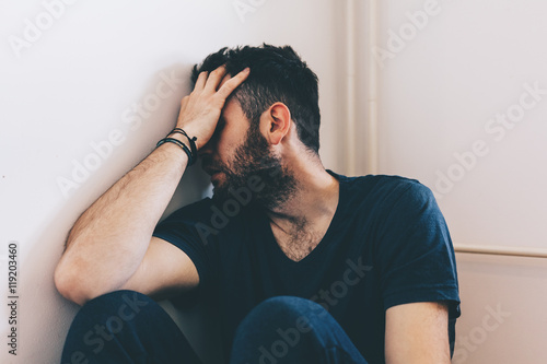 Sad young man sitting in the corner of the room
 photo