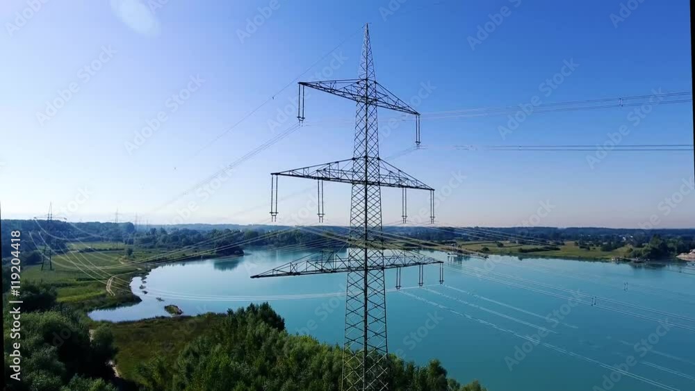 Video von einer Überland Stromleitung mit Kabeln vor einem blauen See in der Natur von unten nach oben
