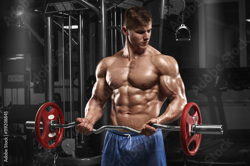Muscular man working out in gym doing exercises with barbell at biceps, strong male naked torso abs