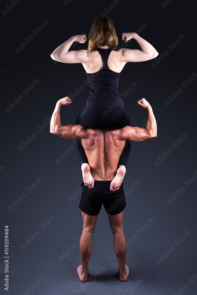 sport concept - sporty woman sitting on shoulders of muscular ma