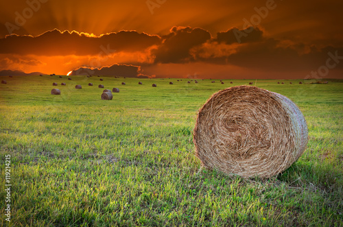 Dramatic sunset in magical countryside with hilly field and rolls of haystack