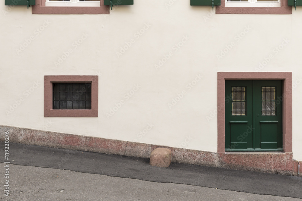 Eine weisse Wand mit einer kleinen grünen Tür und pinkfarbenem Rahmen auf  der rechten Bildhälfte und einem kleinen Fenster auf der linken Bildhälfte.  Stock Photo | Adobe Stock